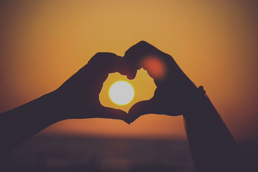 Hands making a heart silhouette in the sunset